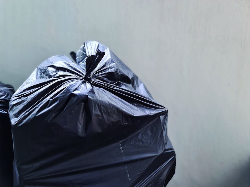 A pile of discarded cardboard boxes, some flattened and others partially intact, resting against a rough brick wall outdoors. The boxes vary in size and are made of brown corrugated cardboard, with so